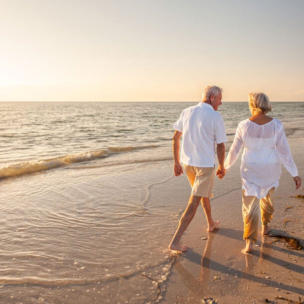 An older couple walking barefoot along the shoreline at sunset